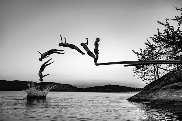 Actionaufnahme in Zug: Silhouetten beim Sprung vom Sprungbrett in den See, Schwarzweissbild