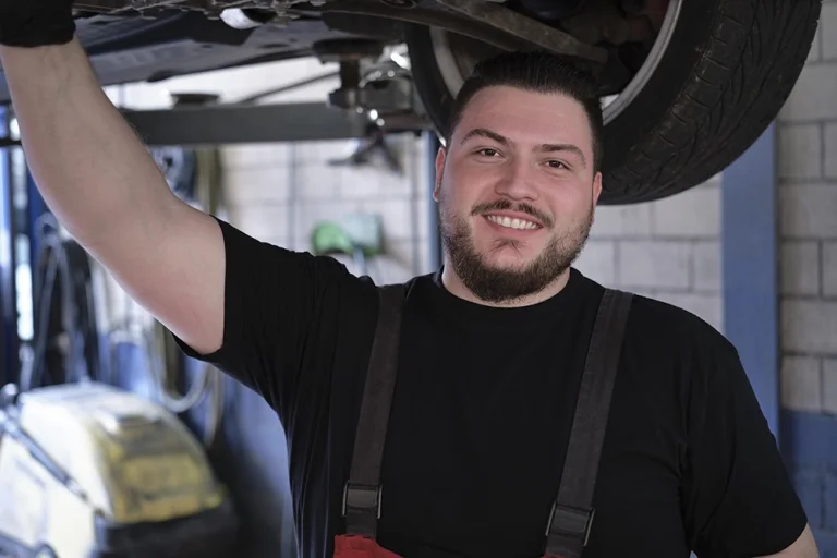 Mitarbeiterfoto in Zug: Automechaniker arbeitet lächelnd unter einem Fahrzeug