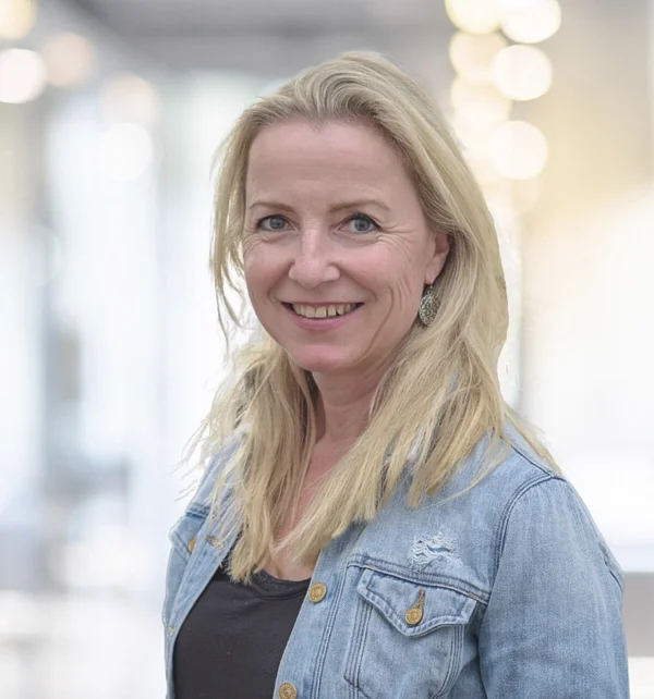 Mitarbeiterportrait in Zug: Frau in Jeansjacke vor hellem, unscharfem Hintergrund